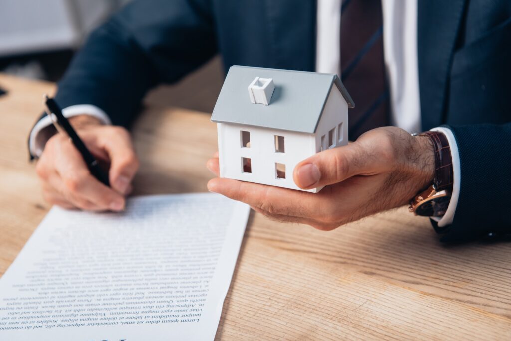 cropped view of lawyer holding house model while signing documents on table