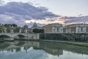 Ornate buildings and bridge reflecting in still river, Rome, Italy